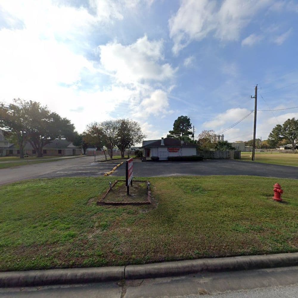 Vacant commercial lot with grassy area, fire hydrant, and nearby trees under a cloudy sky.