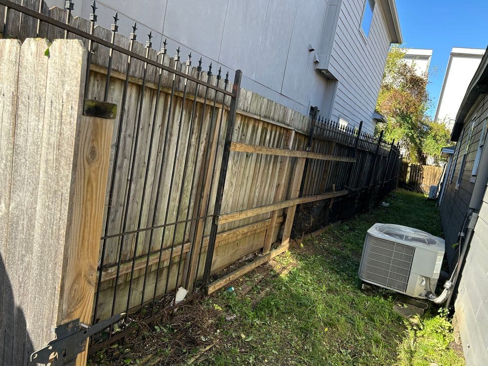 Narrow yard space between homes with wooden and metal fencing, featuring an air conditioning unit.
