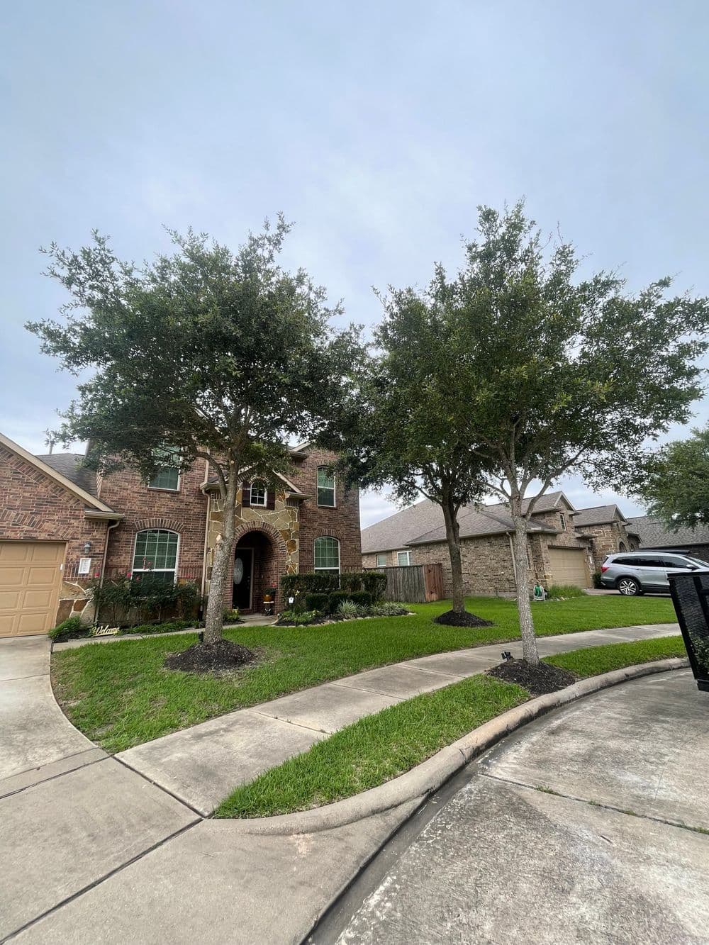 Brick home with lush landscaping and two trees in the front yard on a quiet street.