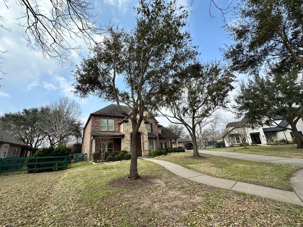 Brick house surrounded by trees and lawns on a quiet neighborhood street.