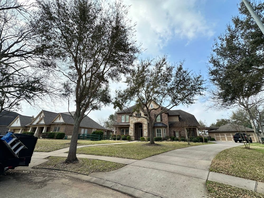 Beautiful brick house with manicured lawn and trees on a sunny residential street.
