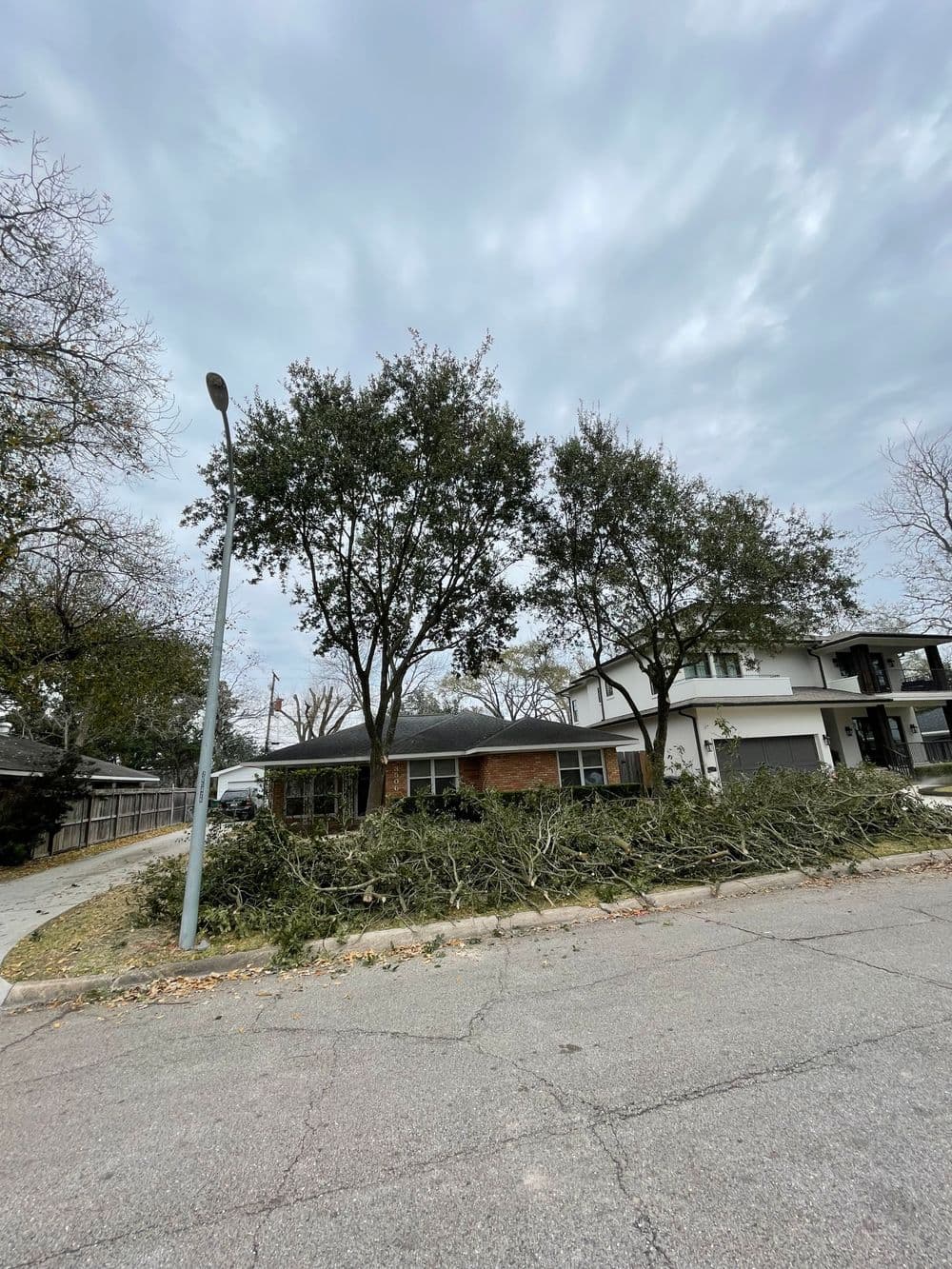 Tree debris piles in front of a house under cloudy sky in a residential neighborhood.