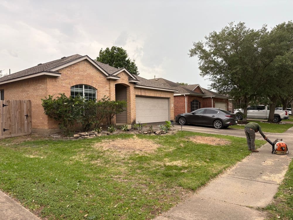 Home exterior with brick facade, man using lawn equipment, and neighboring houses.