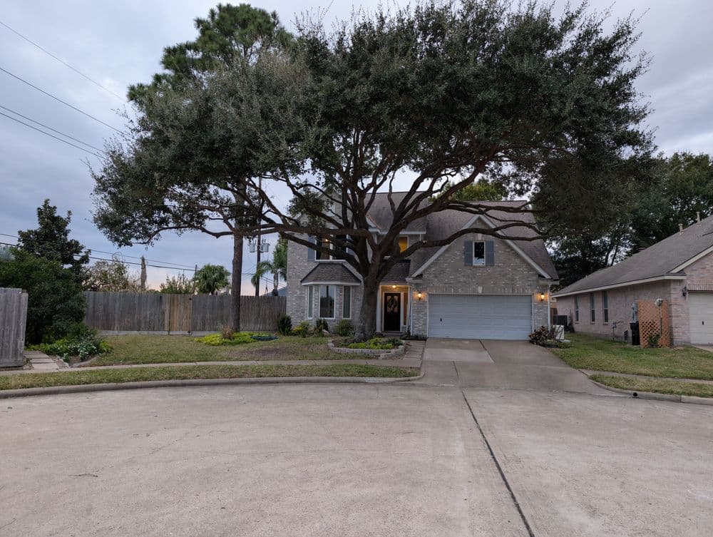 Two-story house with a large oak tree in front, located on a quiet street with landscaped yard.